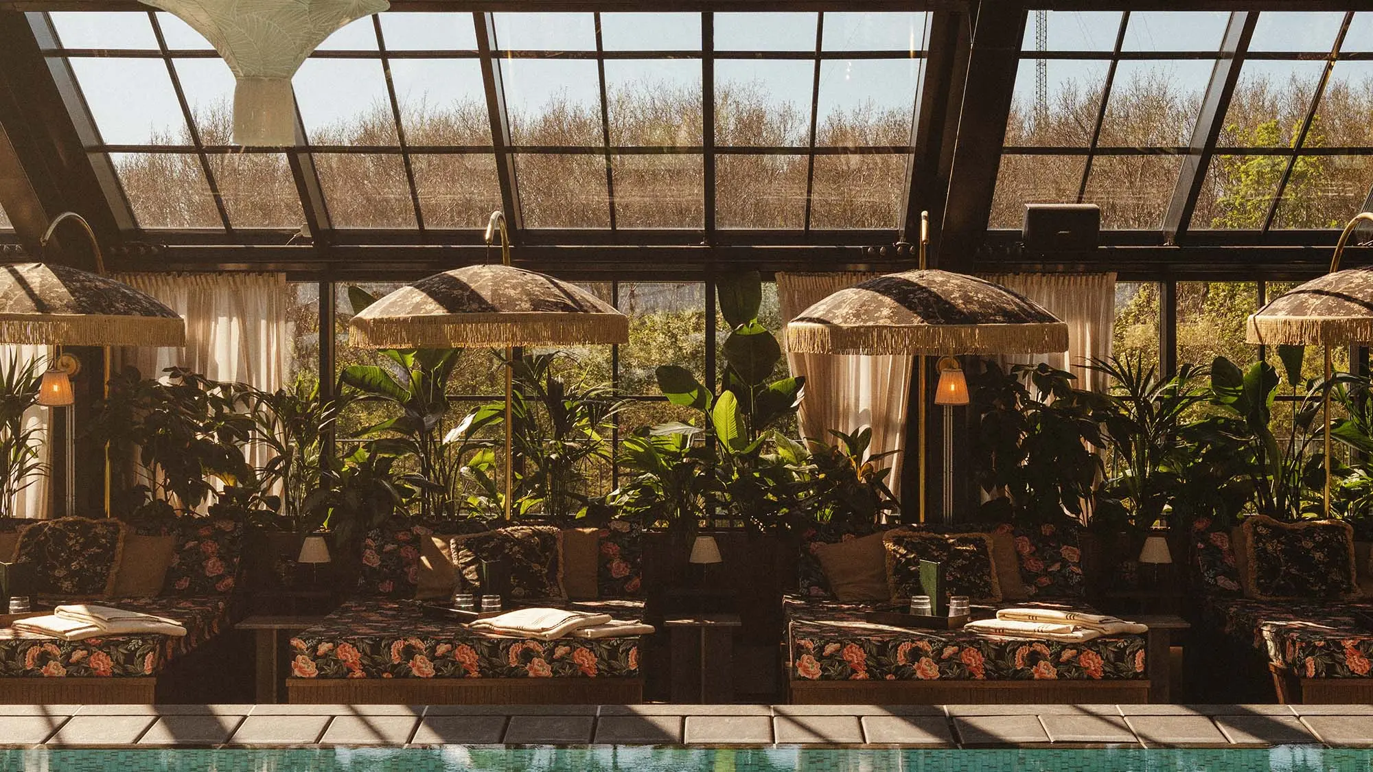 Indoor pool area with floral loungers, tropical plants and a glass ceiling at Rox Resort
